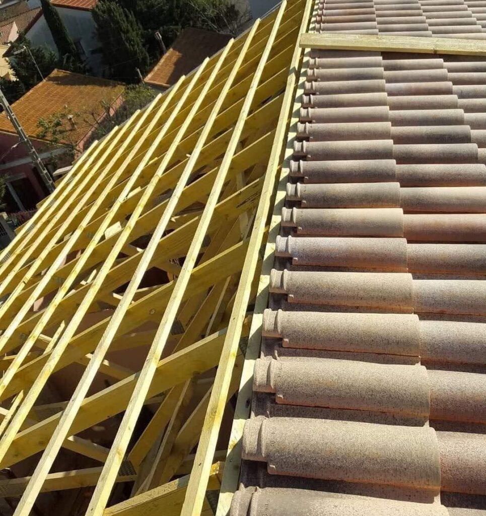 Pose de tuiles en terre cuite sur charpente neuve du toit. Charpente neuve en bois traité et pose de tuiles à emboîtement en terre cuite sur un toit en construction. Vue urbaine méditerranéenne.